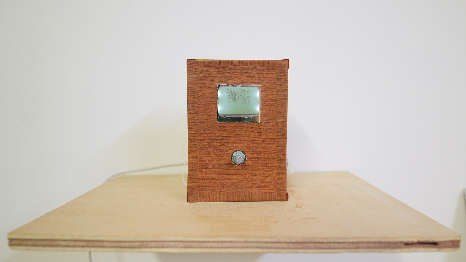 A device covered with fake wood panel wallpaper, with a knob and a screen with glitchy graphics - front view