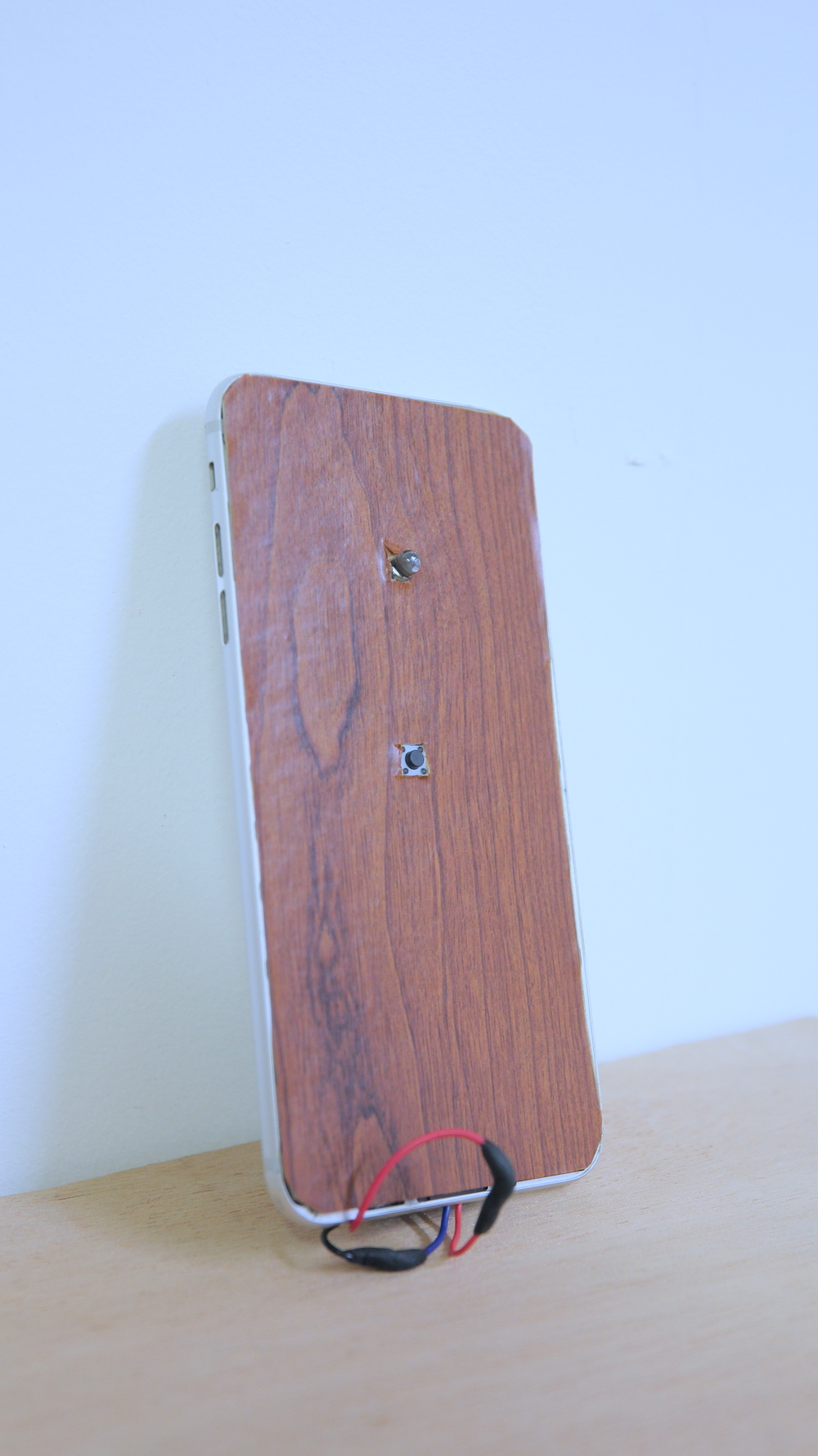An iphone with the screen replaced with fake wood panel wallpaper, a tiny button and a tiny LED light